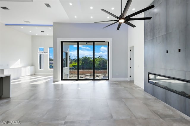 unfurnished room with a fireplace, a towering ceiling, and ceiling fan