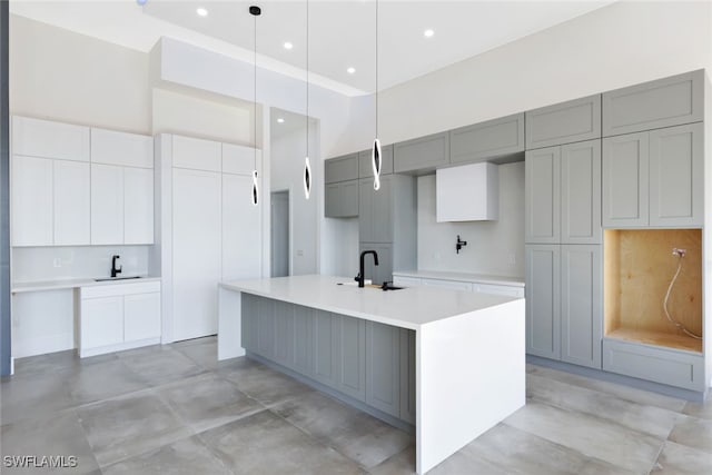 kitchen featuring gray cabinetry, sink, a center island with sink, a high ceiling, and hanging light fixtures