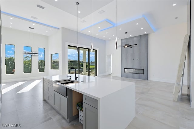 kitchen with a towering ceiling, gray cabinetry, ceiling fan, a large island with sink, and hanging light fixtures