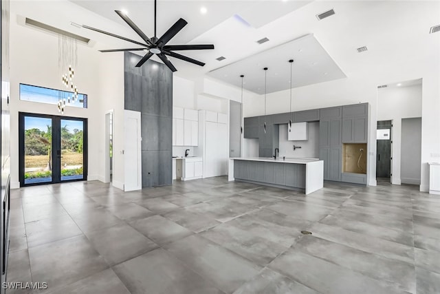 unfurnished living room with ceiling fan with notable chandelier, french doors, a towering ceiling, and concrete floors