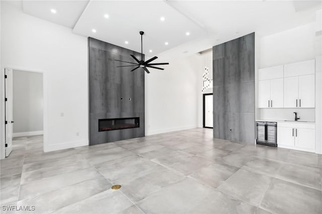 unfurnished living room with wine cooler, a large fireplace, a towering ceiling, and recessed lighting
