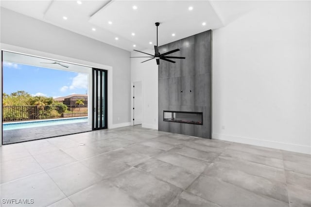 unfurnished living room with a large fireplace, baseboards, a ceiling fan, a high ceiling, and recessed lighting