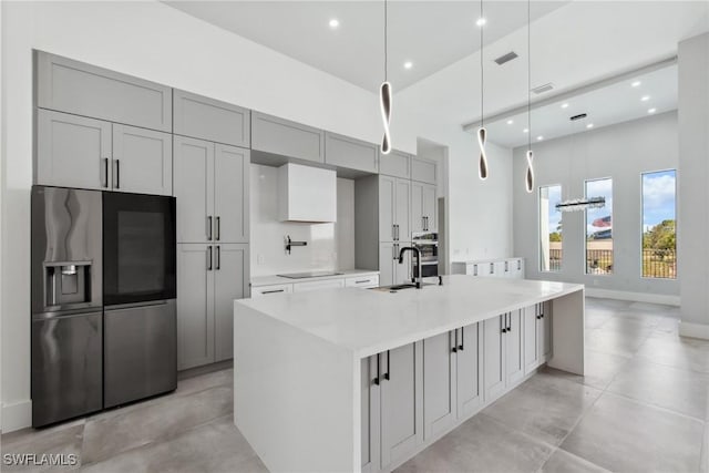 kitchen featuring black electric stovetop, a spacious island, a sink, light countertops, and stainless steel fridge