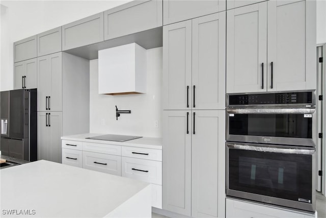 kitchen featuring double oven, light countertops, fridge with ice dispenser, and black electric stovetop