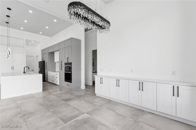 kitchen featuring a high ceiling, a sink, light countertops, gray cabinets, and decorative light fixtures