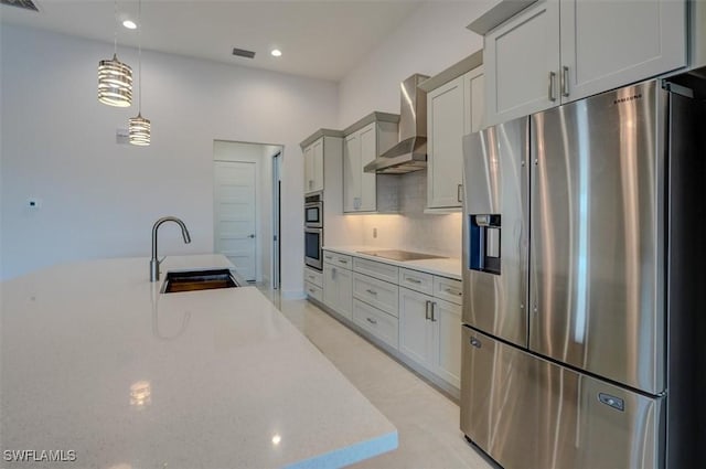 kitchen with pendant lighting, sink, wall chimney exhaust hood, appliances with stainless steel finishes, and tasteful backsplash