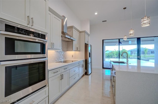 kitchen with decorative backsplash, appliances with stainless steel finishes, wall chimney exhaust hood, sink, and decorative light fixtures