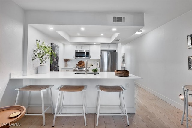 kitchen with a breakfast bar, kitchen peninsula, light hardwood / wood-style flooring, appliances with stainless steel finishes, and white cabinetry