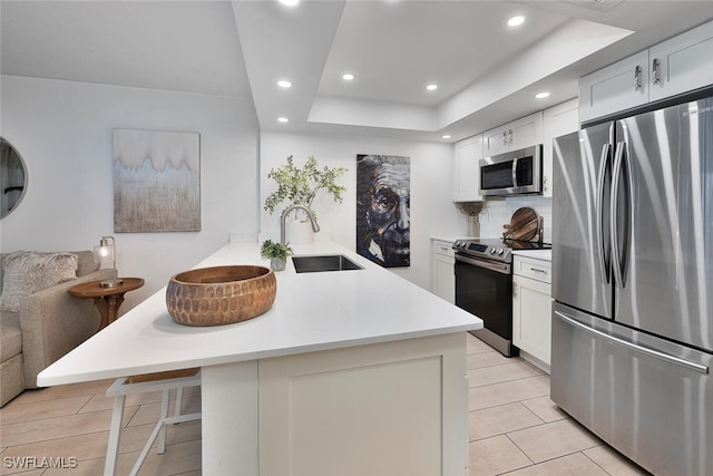 kitchen with a raised ceiling, sink, appliances with stainless steel finishes, white cabinetry, and a breakfast bar area