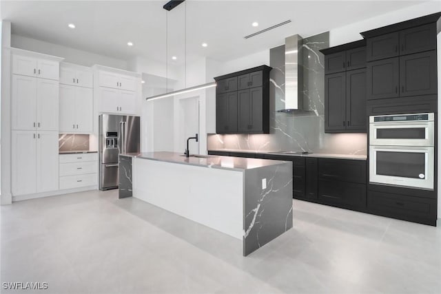 kitchen featuring sink, a kitchen island with sink, white cabinetry, stainless steel appliances, and wall chimney exhaust hood