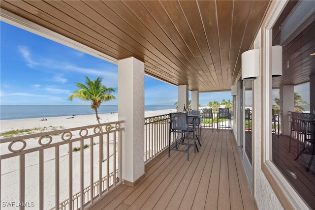 wooden terrace featuring a water view and a beach view