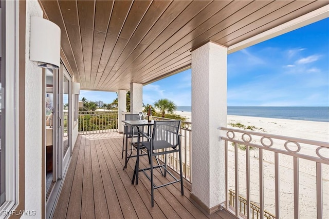 wooden terrace featuring a water view and a beach view