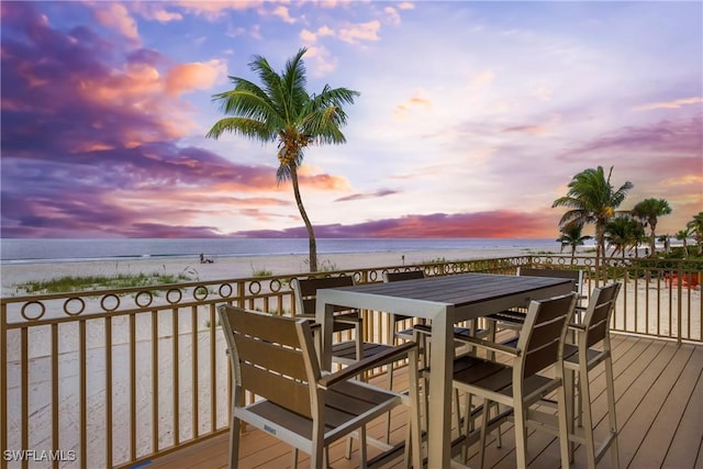 deck at dusk featuring a water view and a beach view