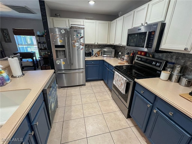 kitchen with stainless steel appliances, light tile patterned floors, blue cabinets, decorative backsplash, and white cabinets