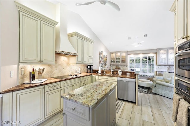 kitchen with kitchen peninsula, stainless steel appliances, lofted ceiling, light stone counters, and sink