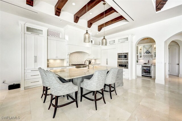 kitchen featuring light stone countertops, beverage cooler, stainless steel appliances, beamed ceiling, and a spacious island