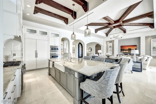 kitchen featuring sink, built in appliances, beamed ceiling, white cabinets, and a large island