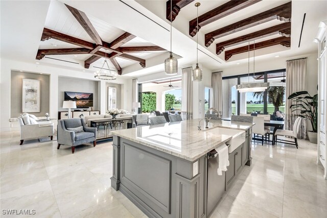 kitchen with pendant lighting, gray cabinetry, ceiling fan with notable chandelier, light stone countertops, and an island with sink