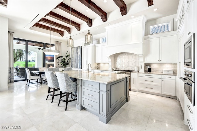 kitchen featuring light stone countertops, appliances with stainless steel finishes, a kitchen island with sink, white cabinets, and hanging light fixtures