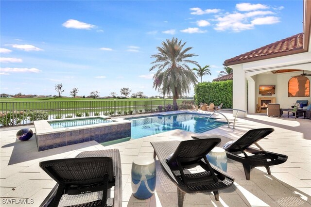 view of swimming pool with a patio area, an in ground hot tub, a water view, and an outdoor fireplace