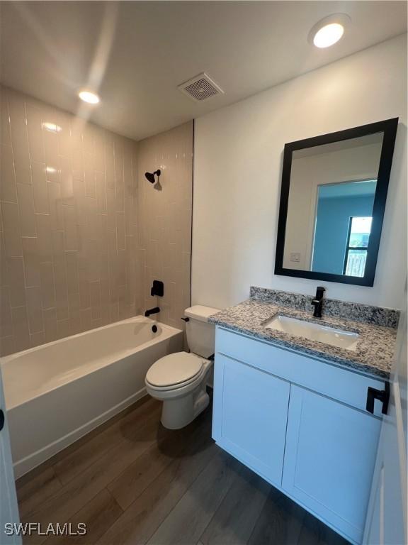 full bathroom featuring wood-type flooring, toilet, tiled shower / bath combo, and vanity