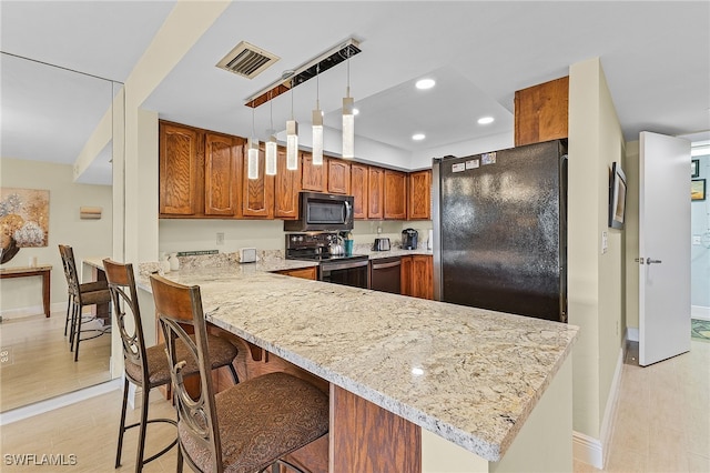 kitchen with kitchen peninsula, light stone countertops, black appliances, hanging light fixtures, and a breakfast bar area