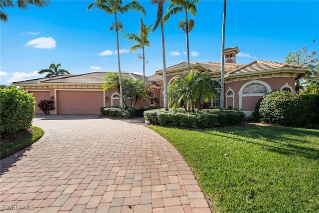 view of front of home featuring decorative driveway, a tile roof, stucco siding, an attached garage, and a front lawn