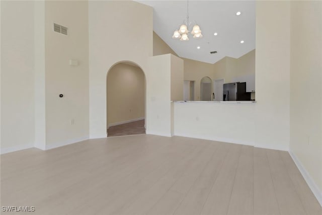 unfurnished living room featuring a notable chandelier, high vaulted ceiling, and light hardwood / wood-style floors