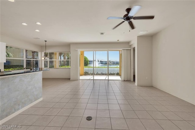 tiled empty room featuring ceiling fan with notable chandelier and a water view