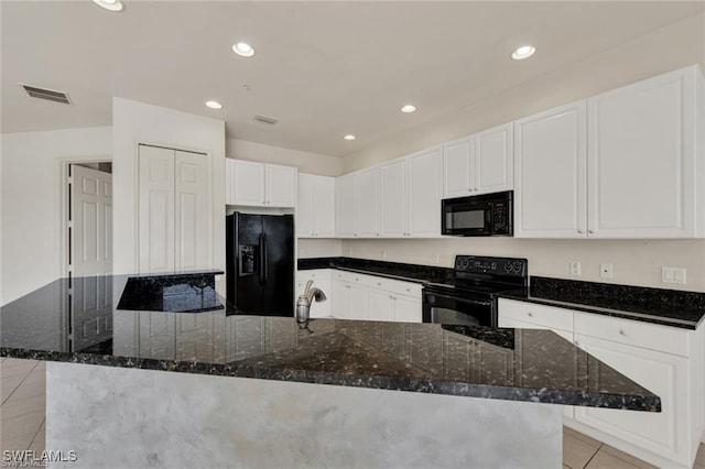 kitchen featuring dark stone counters, black appliances, a large island with sink, light tile patterned floors, and white cabinetry