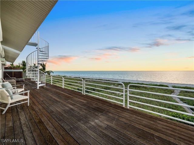 deck at dusk with a water view and a view of the beach