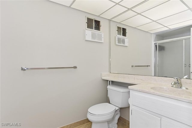 bathroom featuring vanity, a stall shower, a drop ceiling, tile patterned floors, and toilet