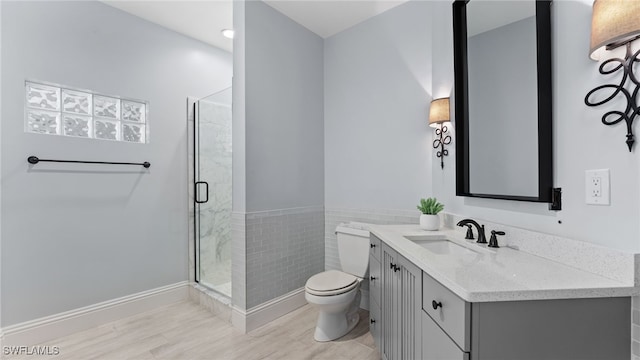 bathroom with wood-type flooring, toilet, vanity, a shower with shower door, and tile walls