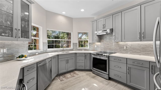 kitchen with backsplash, light stone counters, gray cabinetry, stainless steel appliances, and sink