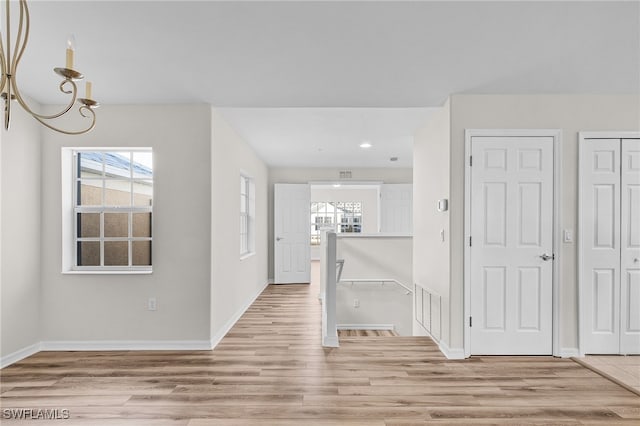 hall with light wood-type flooring and an inviting chandelier