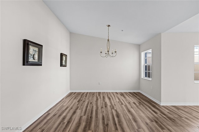 unfurnished dining area featuring a notable chandelier, wood-type flooring, and vaulted ceiling