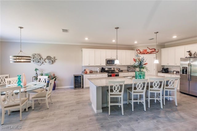 kitchen with white cabinets, wine cooler, an island with sink, appliances with stainless steel finishes, and decorative light fixtures