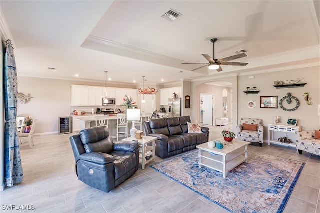 living room featuring ceiling fan, a raised ceiling, ornamental molding, and wine cooler