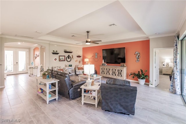 living room featuring ceiling fan, a raised ceiling, ornamental molding, and french doors