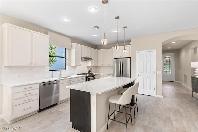 kitchen featuring decorative light fixtures, a center island, appliances with stainless steel finishes, white cabinets, and backsplash