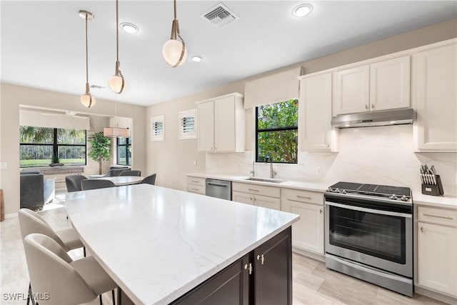 kitchen featuring appliances with stainless steel finishes, pendant lighting, white cabinetry, sink, and a kitchen bar