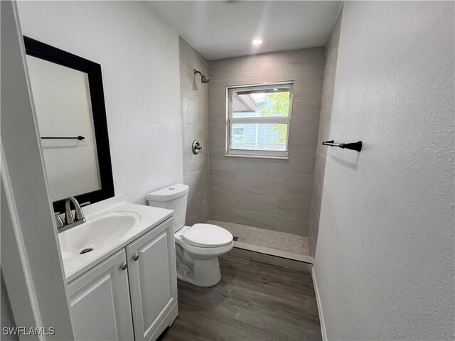 bathroom with a tile shower, toilet, vanity, and wood-type flooring