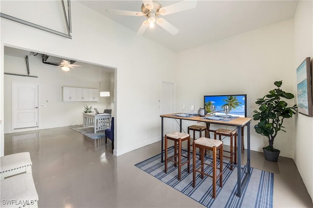 dining room featuring a towering ceiling, concrete floors, and ceiling fan