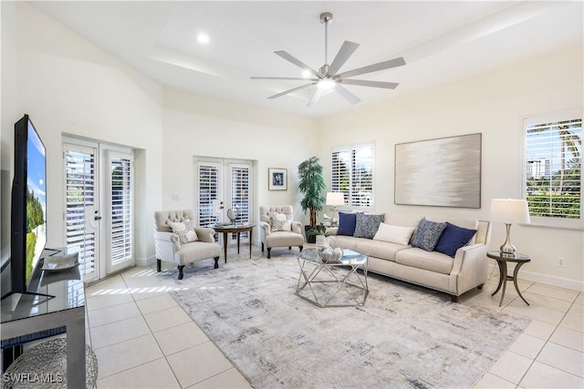 living room with a raised ceiling, light tile patterned floors, french doors, and ceiling fan