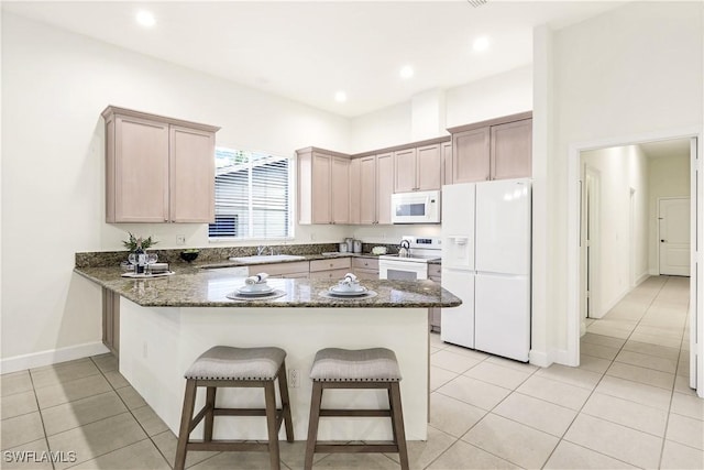 kitchen with light brown cabinetry, white appliances, kitchen peninsula, and dark stone counters