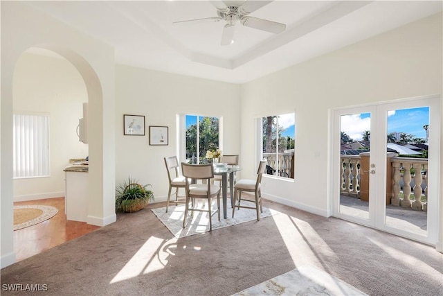 carpeted dining area featuring a raised ceiling, ceiling fan, and french doors