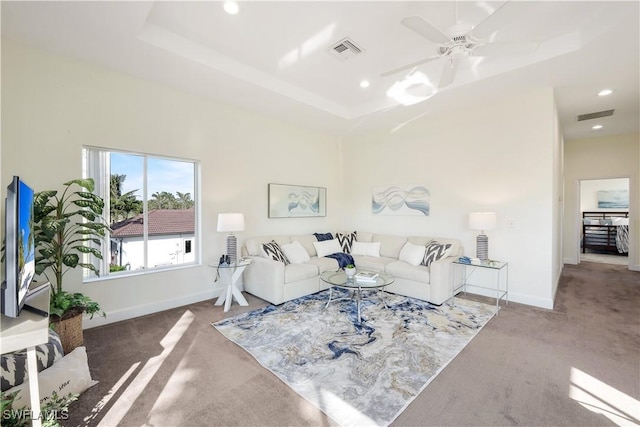 carpeted living room with a raised ceiling and ceiling fan