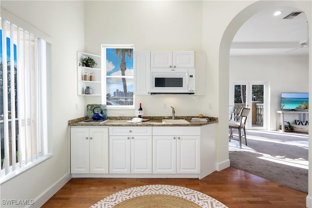 kitchen featuring sink, light hardwood / wood-style floors, dark stone counters, and white cabinets