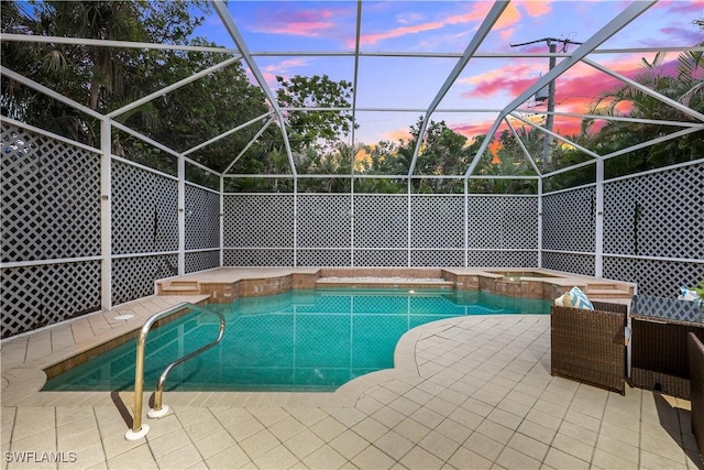 pool at dusk with an in ground hot tub, glass enclosure, and a patio area