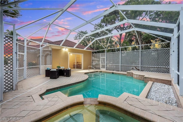 pool at dusk featuring an in ground hot tub, a patio, and glass enclosure